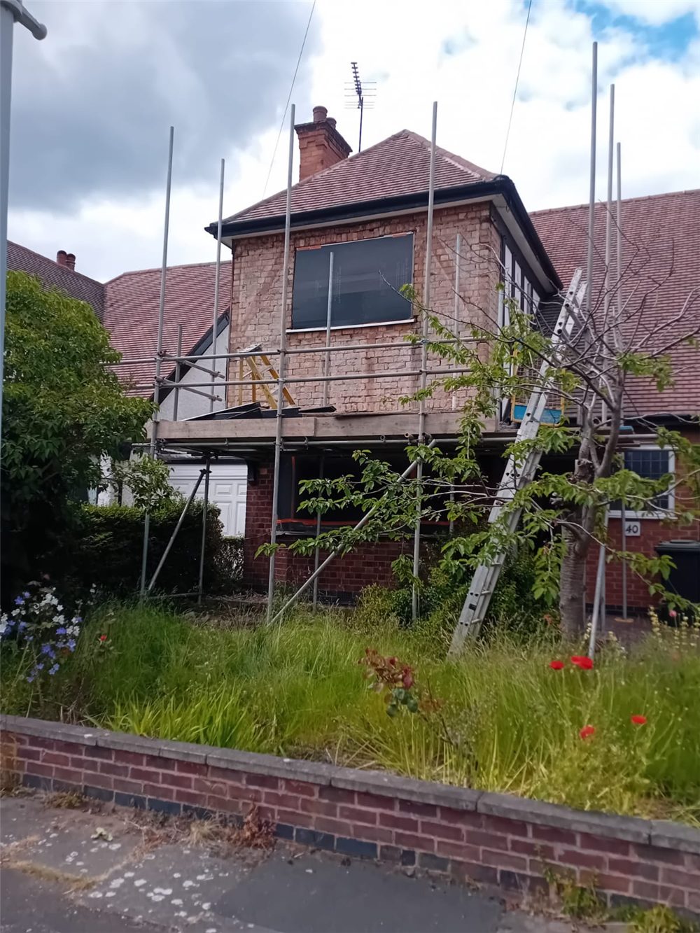 A brick house wrapped in scaffolding during roof and wall work