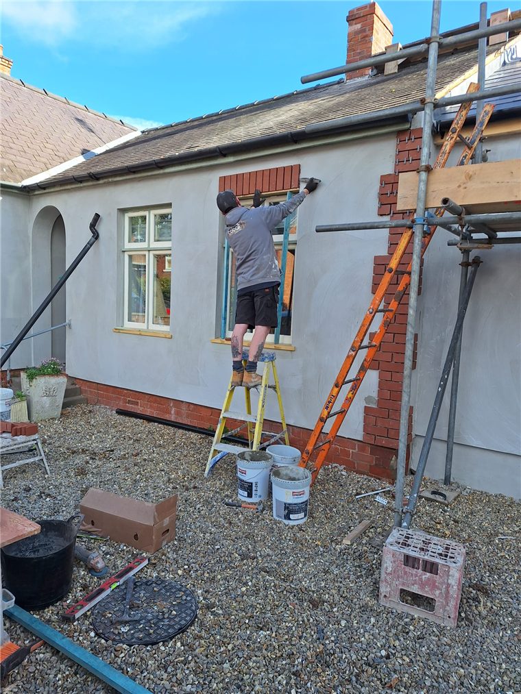 An installer working from a ladder above a window during external works